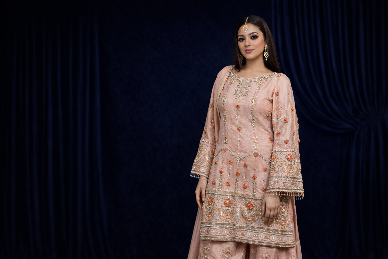 Woman wearing a traditional embroidered outfit against a dark background
